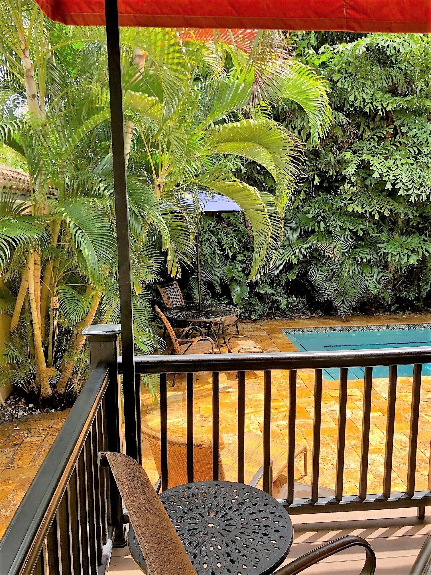 Un balcon avec une piscine, entouré d’une végétation luxuriante et agrémenté d’un parasol rouge.