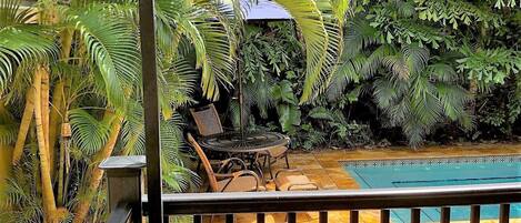Un balcon avec une piscine, entouré d’une végétation luxuriante et agrémenté d’un parasol rouge.
