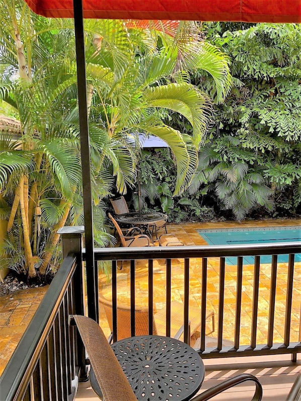 A balcony with a pool, surrounded by lush greenery and a red umbrella. - Clearwater Beach Pool House Rental - Just Steps to the Beach (Clearwater Beach)