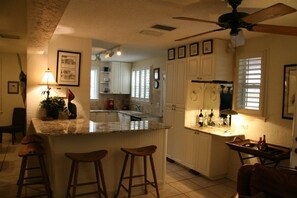 A kitchen with a bar area, white cabinets, a ceiling fan, and a dining area with a table and chairs. - Clearwater Beach Pool House Rental - Just Steps to the Beach (Clearwater Beach)