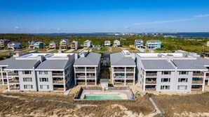 A coastal residential area with modern multi-story buildings, a swimming pool, and a view of the ocean. - DS203 Ocean-Front Condo with Pool and Ocean Views! (Nags Head)
