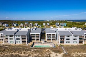 Zona residencial costeira com edifícios modernos de vários andares, piscina e vista para o oceano.
