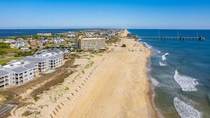 A coastal area with a sandy beach, a pier extending into the water, and residential buildings along the shore. - DS203 Ocean-Front Condo with Pool and Ocean Views! (Nags Head)