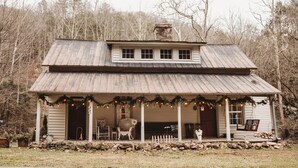 A rustic cabin with a porch, a chimney, and a small front yard.