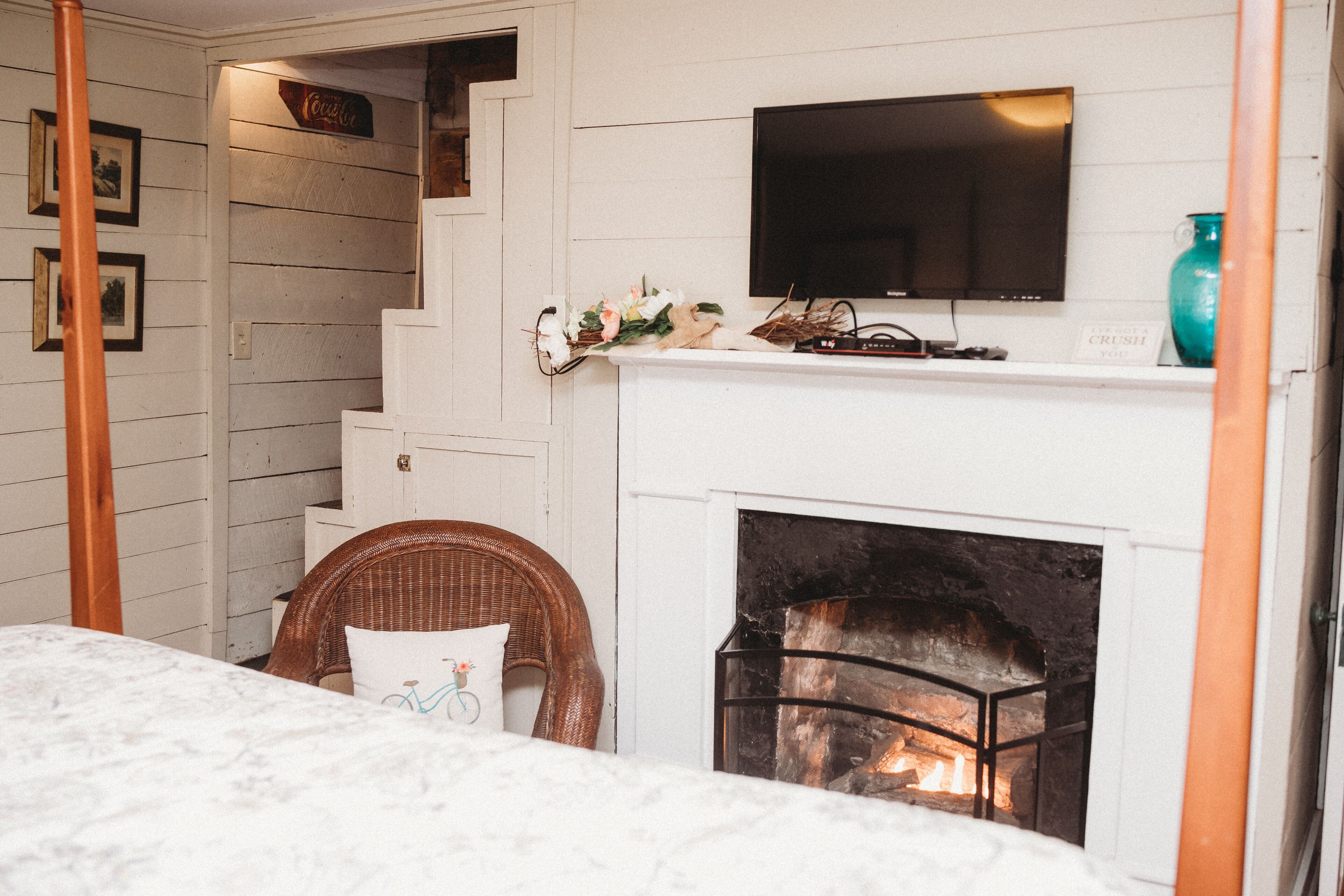 A cozy room with a fireplace, a television mounted above it, and a wicker chair with a cushion.