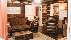 A cozy living room with a brown patterned sofa, a leather armchair, a wooden cabinet, and a vintage suitcase.