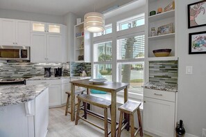 A modern kitchen with white cabinetry, a built-in microwave, a stainless steel refrigerator, and a wooden dining table with benches.