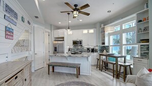 Une cuisine moderne avec des meubles blancs, un îlot central et un ventilateur de plafond.