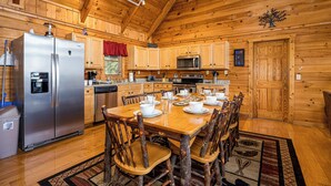 Cocina de cabaña de madera con una mesa de comedor dispuesta para cuatro personas, sillas de madera, un refrigerador, un microondas y armarios de madera.