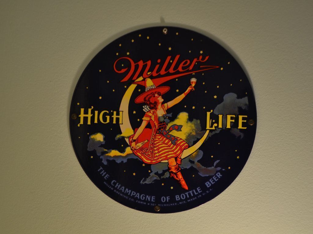 Una señal circular con una mujer sosteniendo una botella, con la etiqueta 'Miller High Life'.