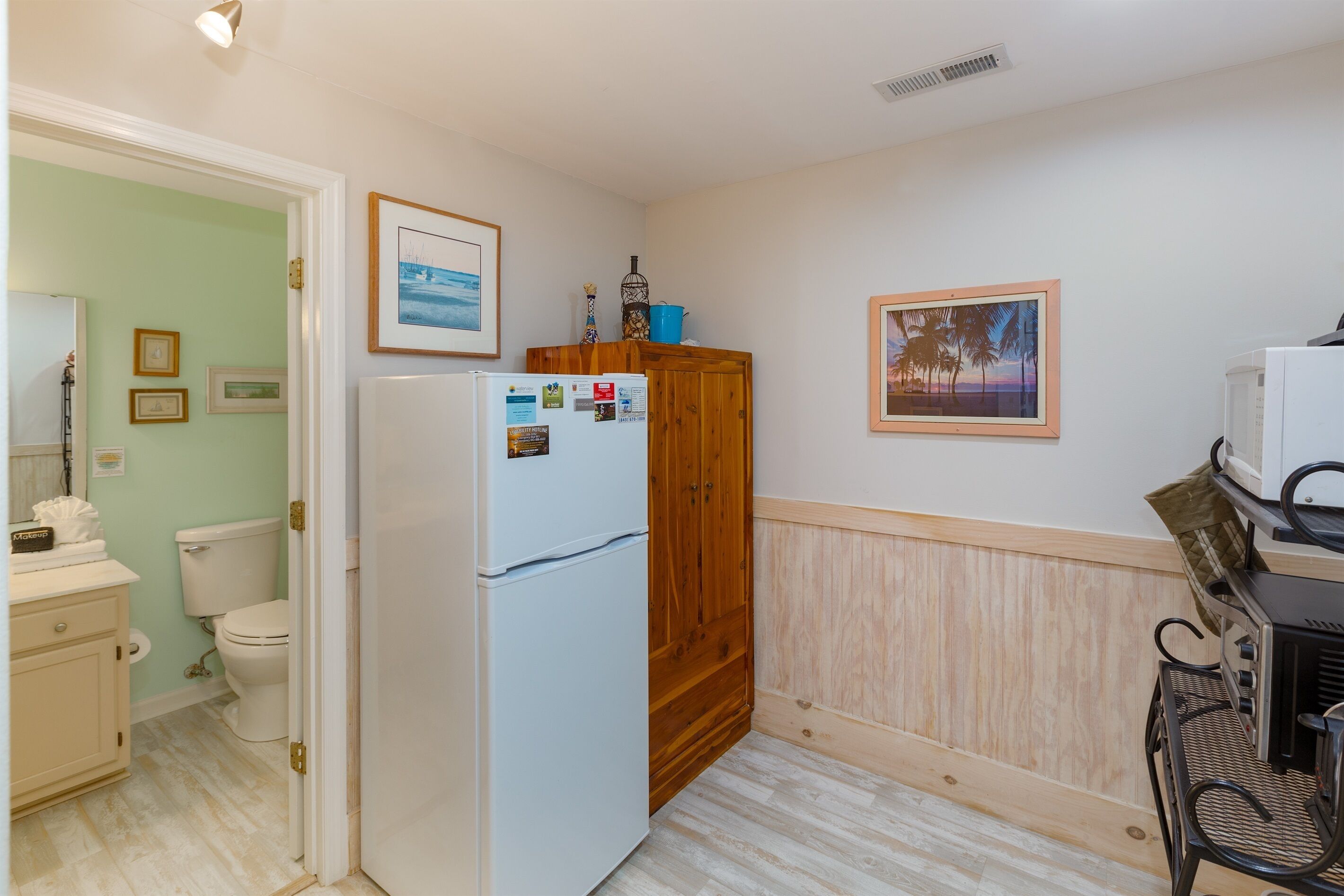 A compact kitchen with a refrigerator, wooden cabinet, and a dining area with a chair.