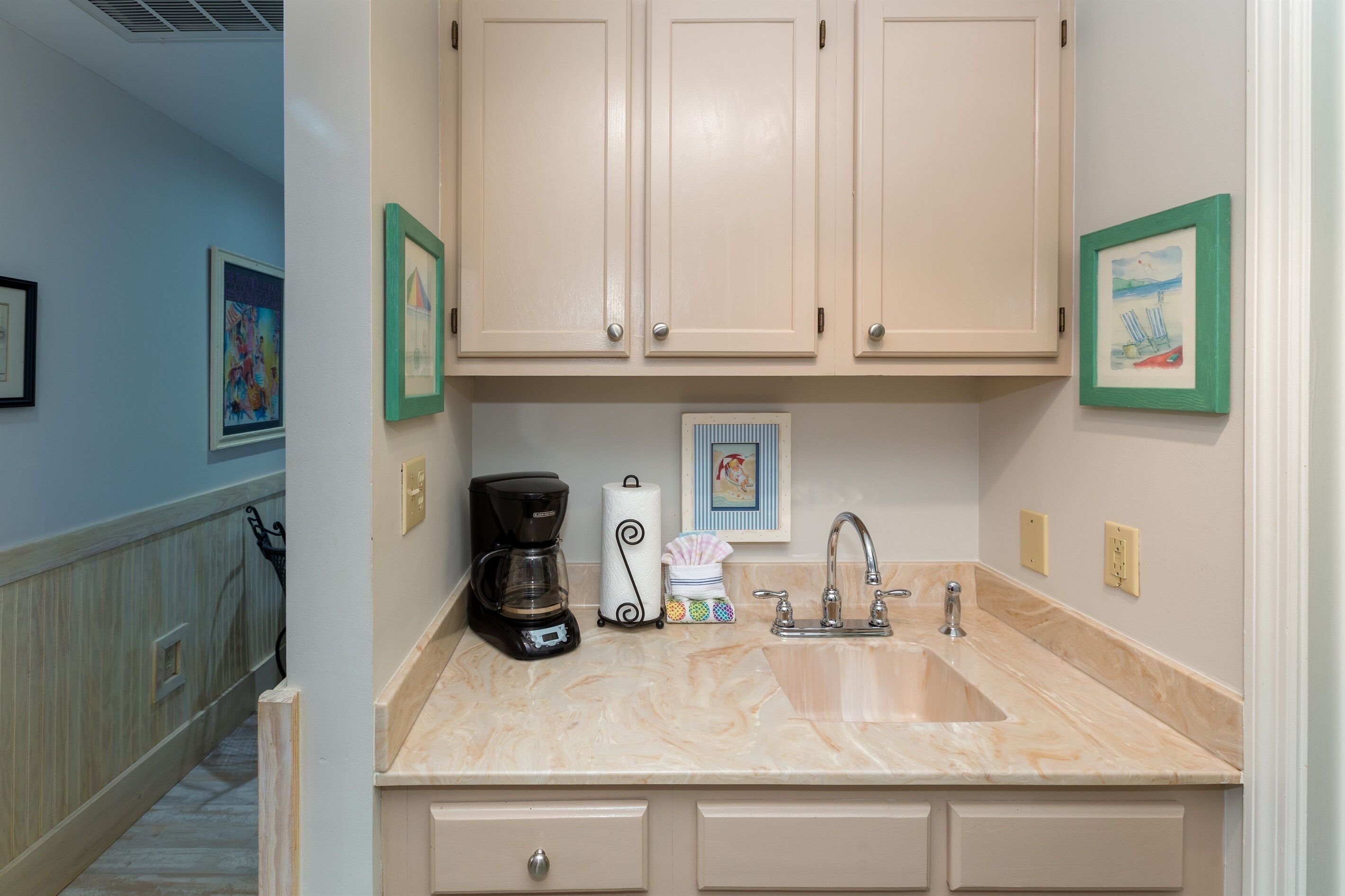 A kitchen with beige cabinets, a marble countertop, a coffee maker, and a sink.