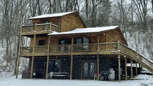 Une cabane en bois à deux étages, dotée d’un balcon et entourée d’arbres couverts de neige.