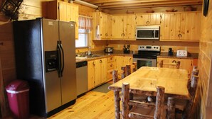 Une cuisine de style rustique, avec des éléments en bois, comprenant un réfrigérateur, un four à micro-ondes, une cuisinière et une table à manger en bois, ainsi que des chaises.
