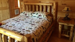 Un lit en bois avec une couvre-lit à motifs, une table de chevet avec une lampe et une fenêtre avec un rideau rouge.