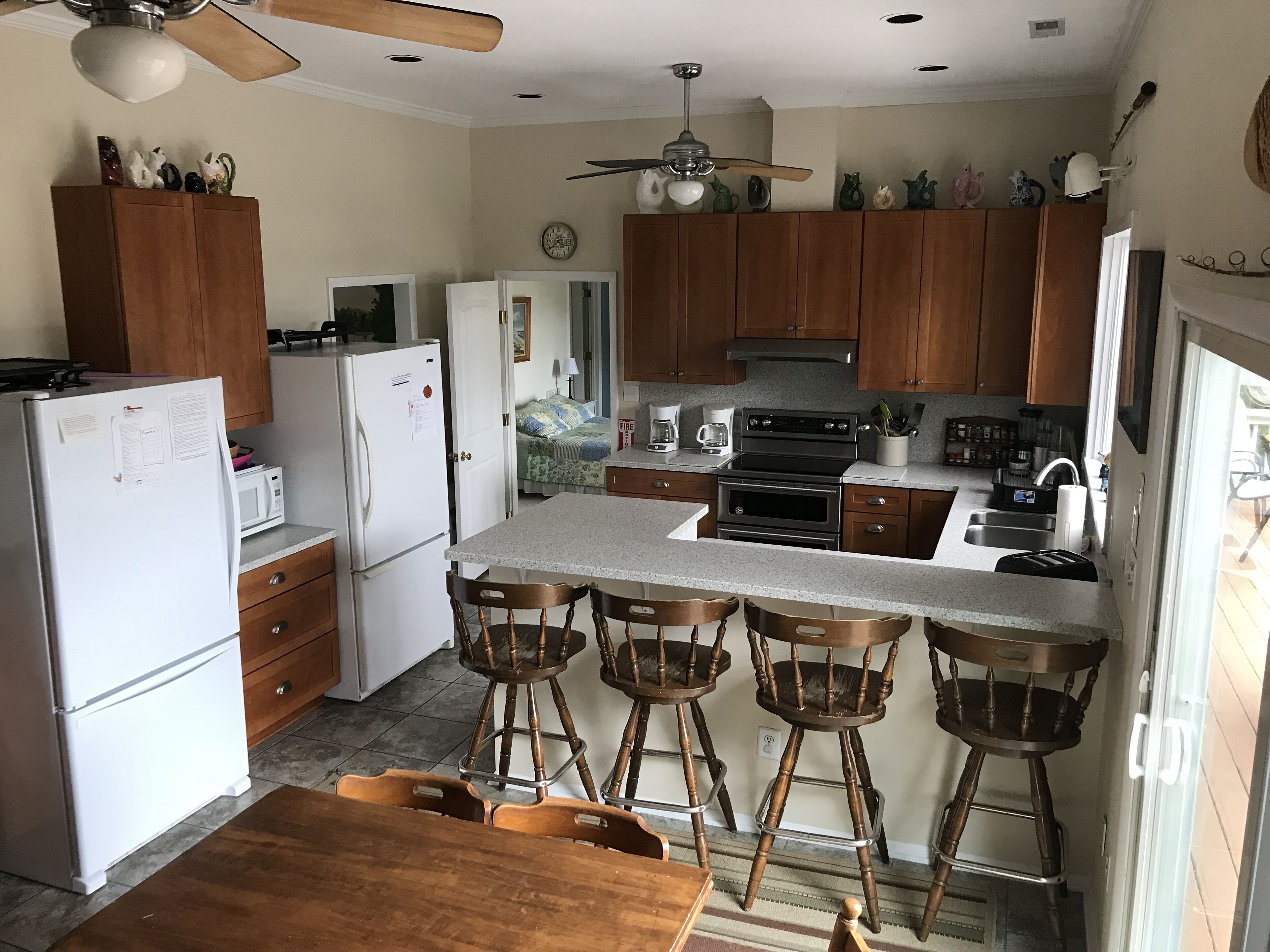 Une cuisine avec des meubles de rangement en bois, un réfrigérateur, un four à micro-ondes, une cuisinière et des tabourets de bar.