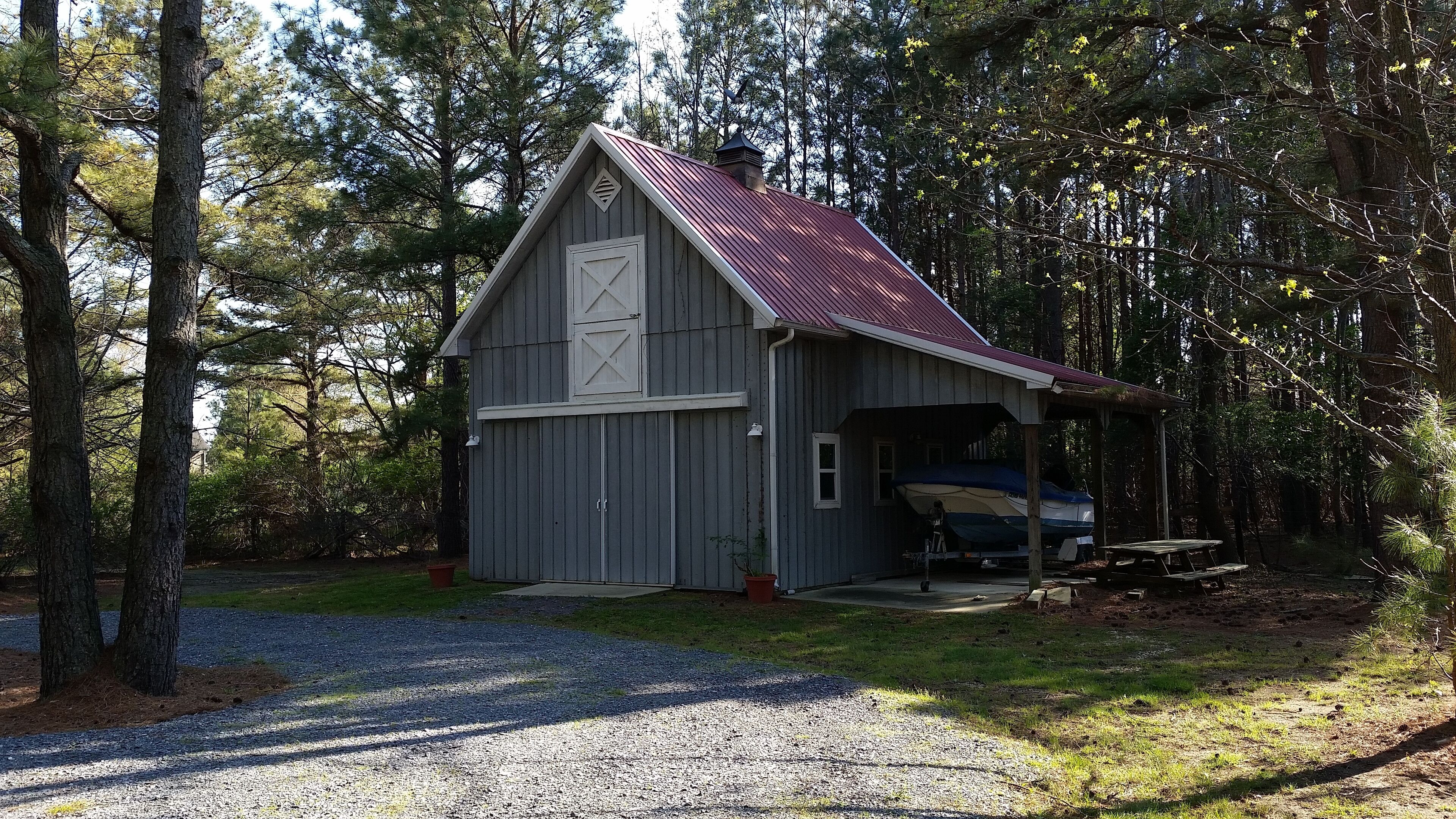 A rustic cabin with a red roof, a garage, and a covered boat storage area.