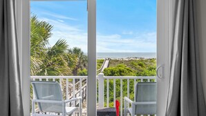 Ein Balkon mit zwei weißen Stühlen, einem Tisch und Blick auf das Meer und den Strand.