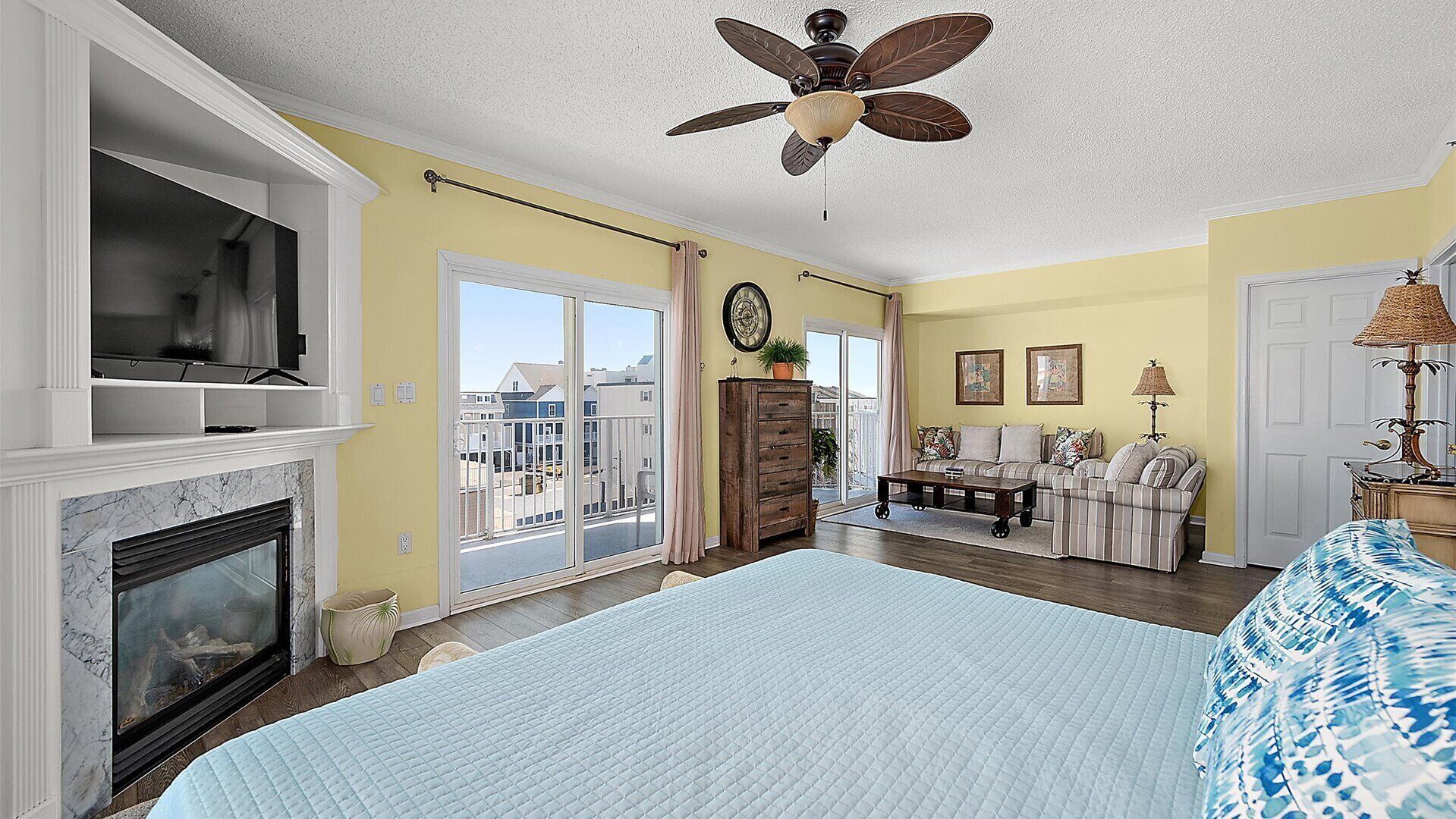 A spacious bedroom with a large bed, a fireplace, a ceiling fan, and a view through the sliding glass doors.