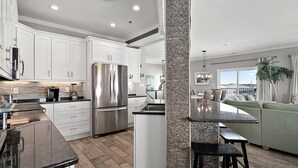 A modern kitchen with white cabinets, a stainless steel refrigerator, and a stone accent wall. - 🏖️ 5 Bedroom Penthouse Ocean Views, Renovated, Pool, Stunning Ocean Views🏖️ (Ocean City)