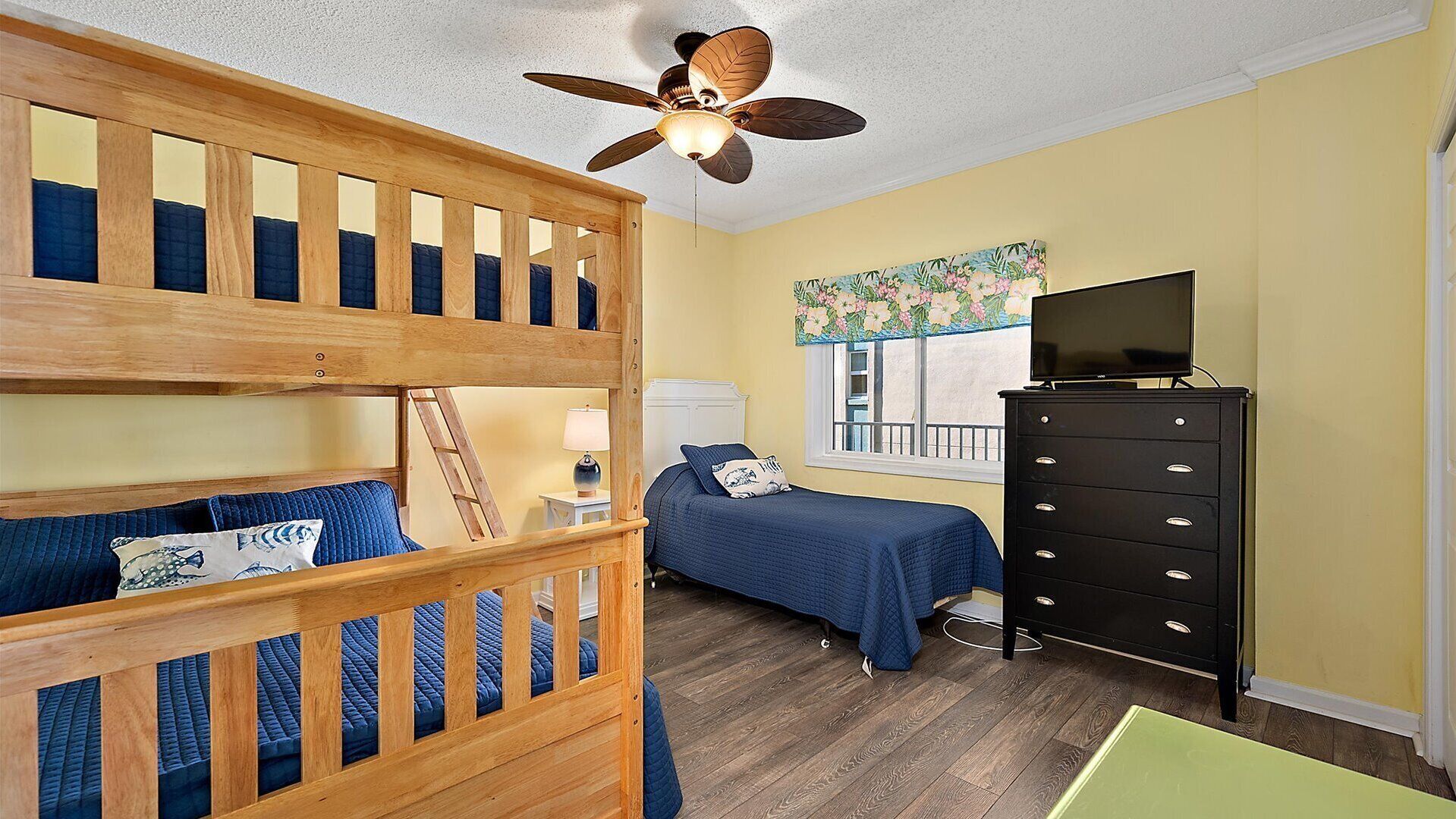 A room with bunk beds, a desk, a dresser, and a ceiling fan.