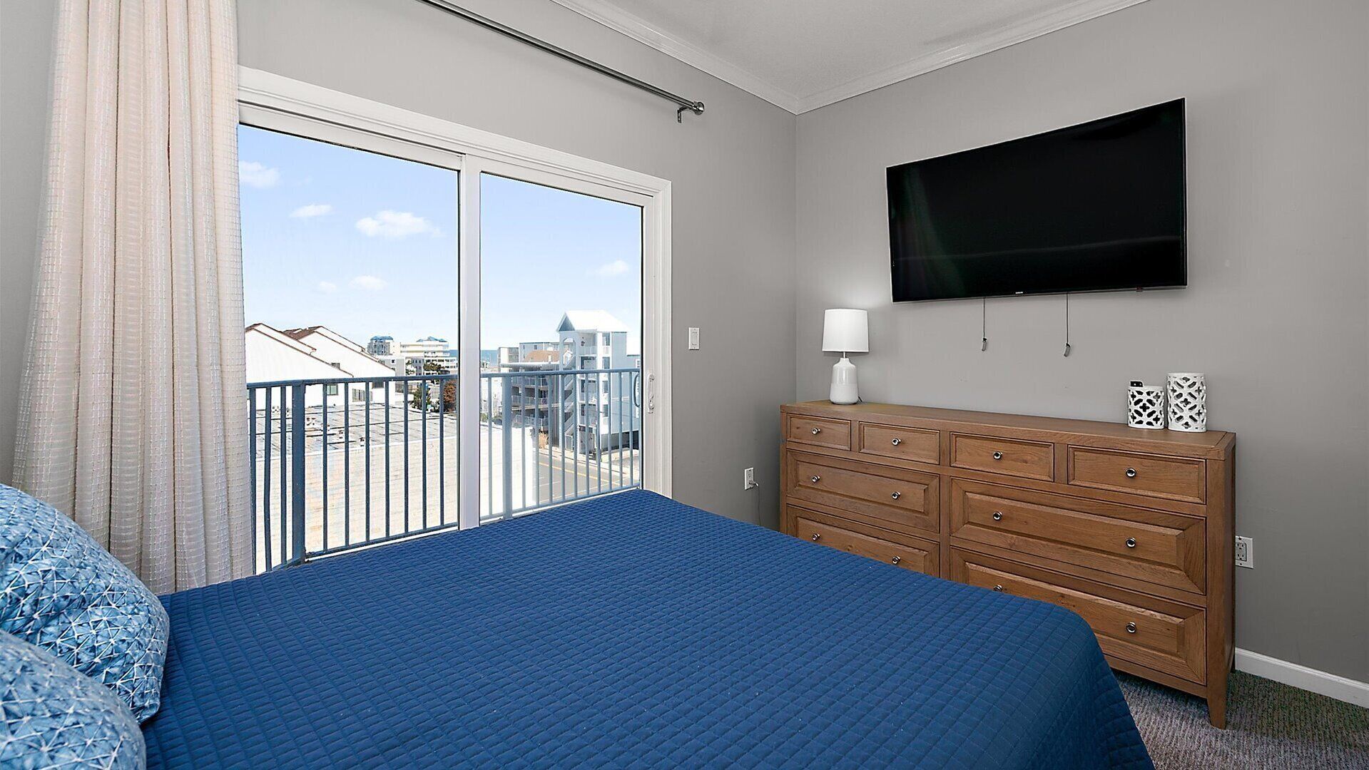 Una camera da letto con un letto grande, una cassettiera, una TV e un balcone con vista sulla città.