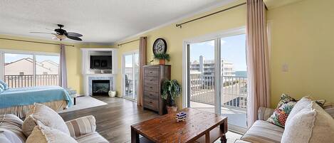 A spacious living room with a fireplace, a ceiling fan, and a view of the ocean through large sliding glass doors.