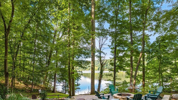 A lakeside patio with Adirondack chairs, a fire pit, and a stone pathway.