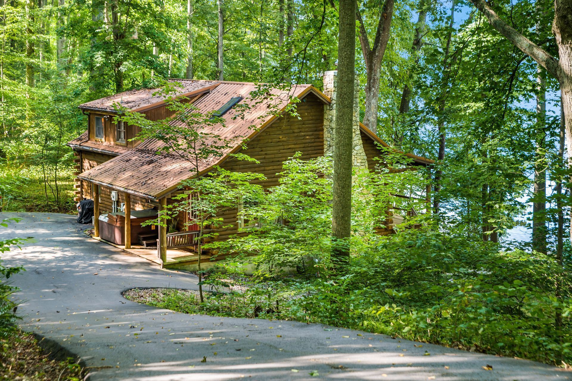 Un chalet rustique doté d’un porche, entouré d’une forêt dense et accessible par un sentier sinueux.