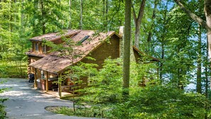 A rustic cabin with a porch, surrounded by dense forest and a winding path leading to it.