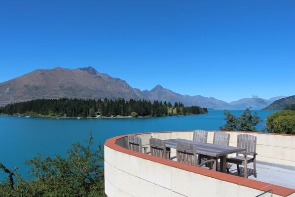 A terrace with a table and chairs overlooking a lake and mountains. - Lakefront Vacation Home (Queenstown)