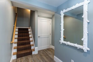 Un escalier avec une main courante recouverte de moquette, une porte blanche et un miroir mural doté d’un cadre original.