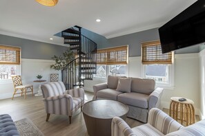 A modern living room with a spiral staircase, a large sofa, striped armchairs, and a round coffee table. - 4 Balconies, Water Views, Fireplace, Kitchen - Great For Groups (Newport)