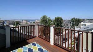 A balcony with a wooden floor and railing, overlooking a residential area with houses and a clear sky. - 4 Balconies, Water Views, Fireplace, Kitchen - Great For Groups (Newport)
