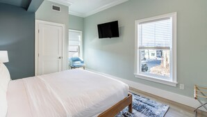 A bedroom with a bed, a TV mounted on the wall, a window with blinds, and a door. - 4 Balconies, Water Views, Fireplace, Kitchen - Great For Groups (Newport)
