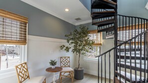 A room with a spiral staircase, a potted tree, two wicker chairs, a small table, and a window with blinds. - 4 Balconies, Water Views, Fireplace, Kitchen - Great For Groups (Newport)