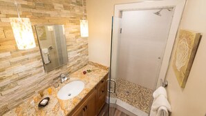 Une salle de bain avec un mur en pierre, une douche en verre et un lavabo en marbre.