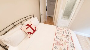 Une chambre à coucher avec un lit, une porte donnant sur une salle de bain et une vue sur la plage par une fenêtre.