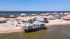 Uma área costeira com várias casas de praia sobre palafitas, uma praia de areia e vista clara do oceano.