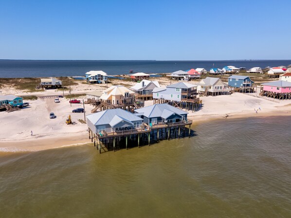 A coastal area with multiple beach houses on stilts, a sandy beach, and a clear view of the ocean.