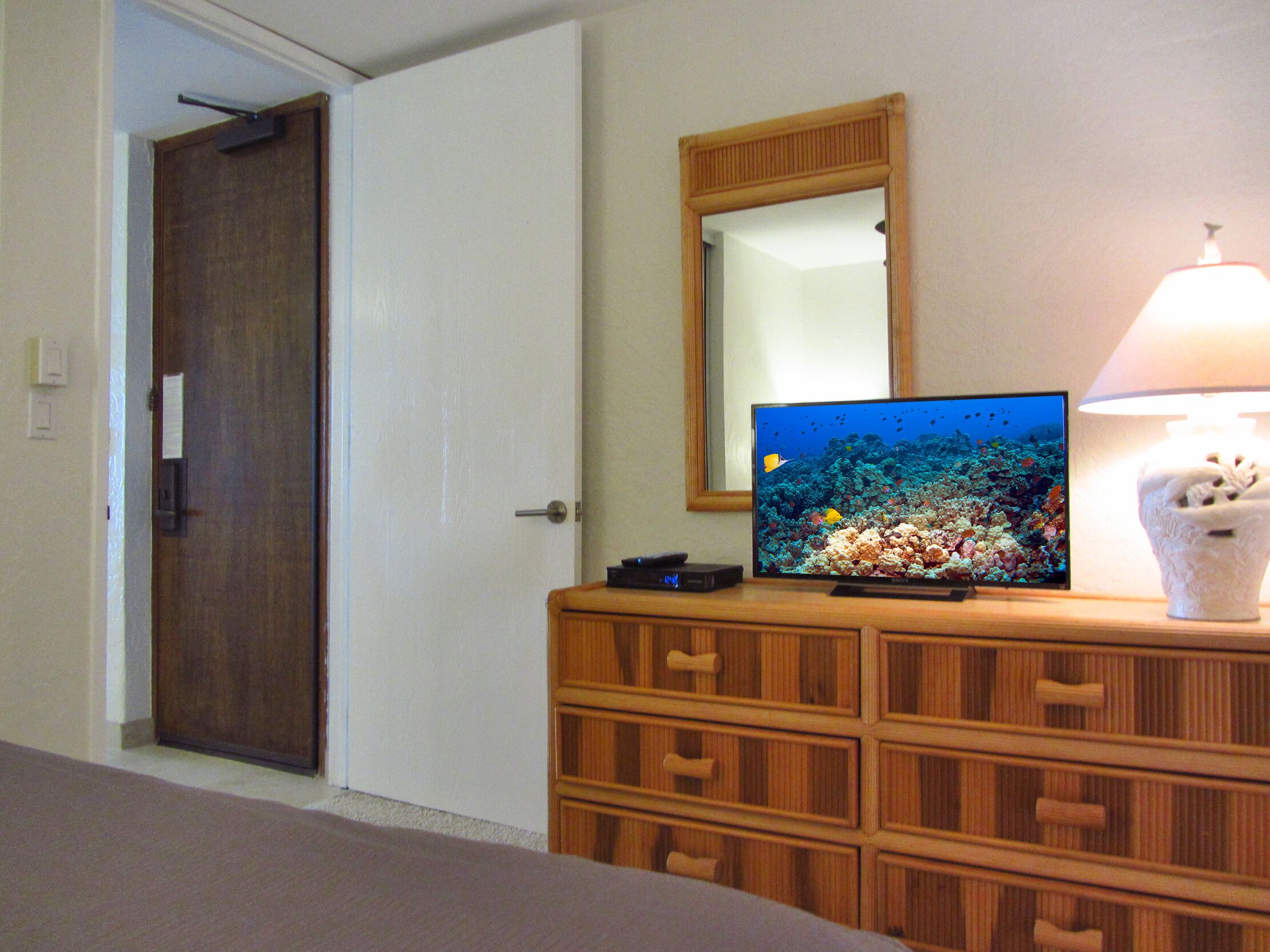 Una habitación con un aparador de madera, un televisor que muestra una escena submarina, una lámpara y una puerta.