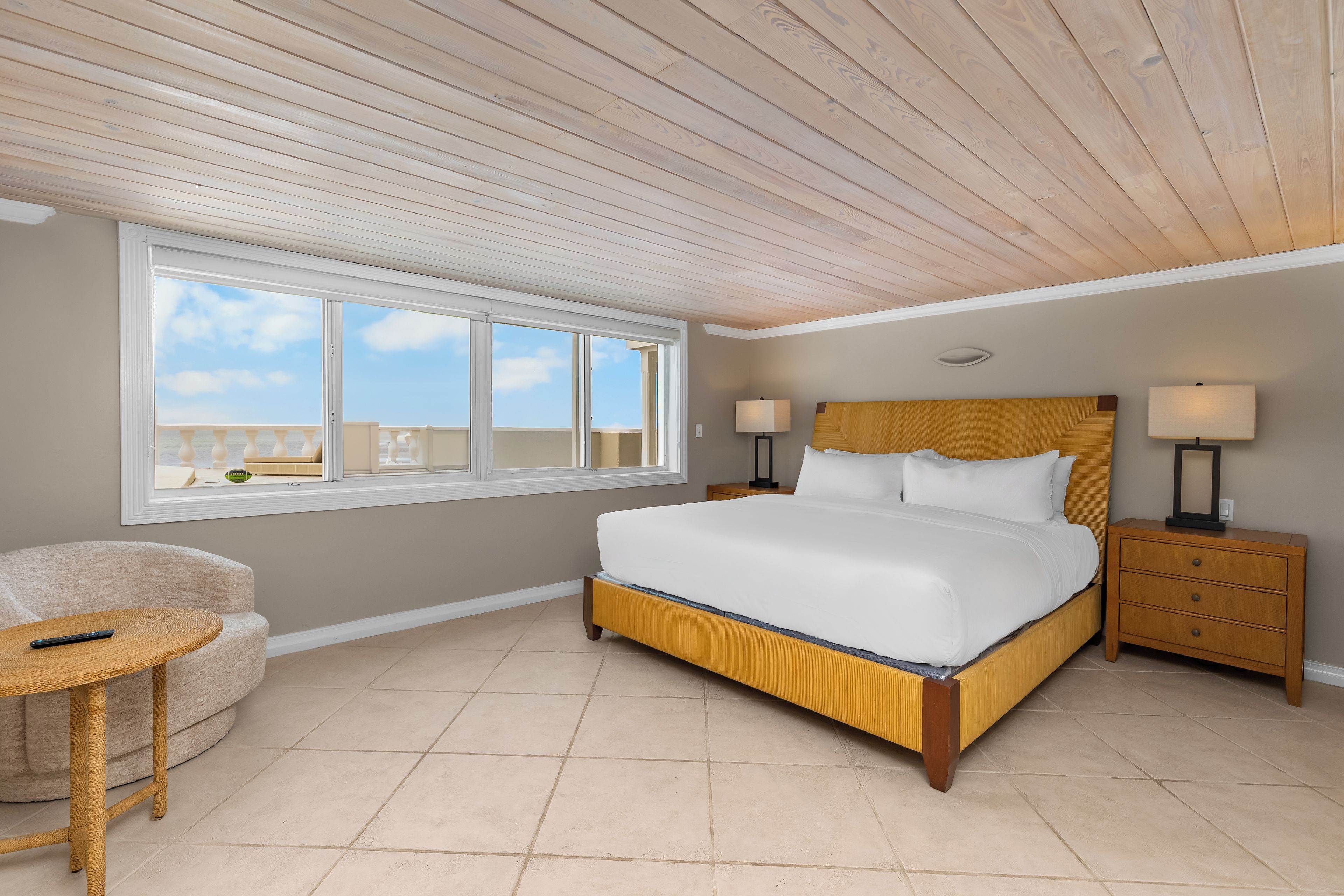 A bedroom with a large bed, a nightstand, a lamp, a chair, and a window with a view.