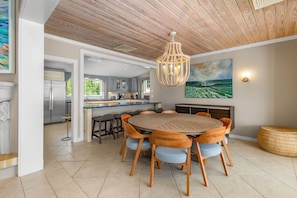 A modern kitchen with a central island, a dining area with a round table and chairs, and a large painting on the wall. - Private Cable Beach villa with pool, oceanfront terrace & guest cottage (Cable Beach, Nassau)