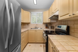 A kitchen with beige cabinets, a stainless steel refrigerator, a built-in oven, and a microwave. - Private Cable Beach villa with pool, oceanfront terrace & guest cottage (Cable Beach, Nassau)