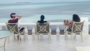 Three people seated on white chairs with a view of the ocean and a distant island. - Luxury Beach--front house, perfect location! Cable Beach BEAUT! Walk to Baha Mar (Cable Beach, Nassau)