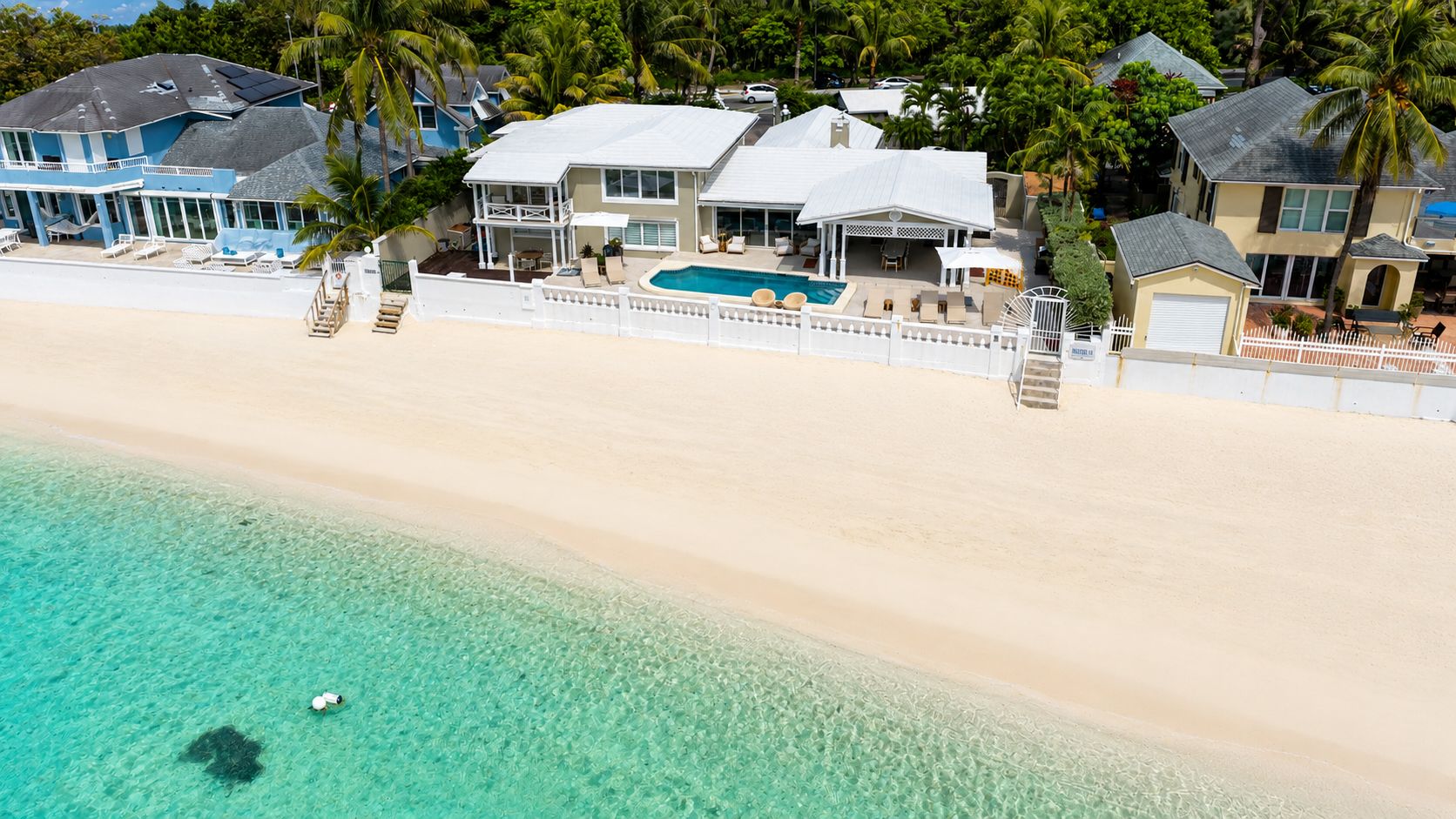 A beachfront property with a swimming pool, multiple houses, and a sandy beach.