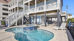A pool area with a hot tub, lounge chairs, and a staircase leading to upper floors. - One Happy Place, Luxury Oceanfront House in Cherry Grove, Pool and Spa (North Myrtle Beach)