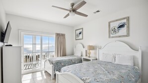 A bedroom with two beds, a ceiling fan, a window with a view, and artwork on the walls. - One Happy Place, Luxury Oceanfront House in Cherry Grove, Pool and Spa (North Myrtle Beach)