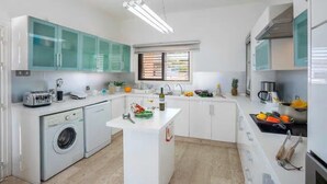 Een kleine keuken met een wasmachine, een centraal kookeiland en een raam met zonwering.