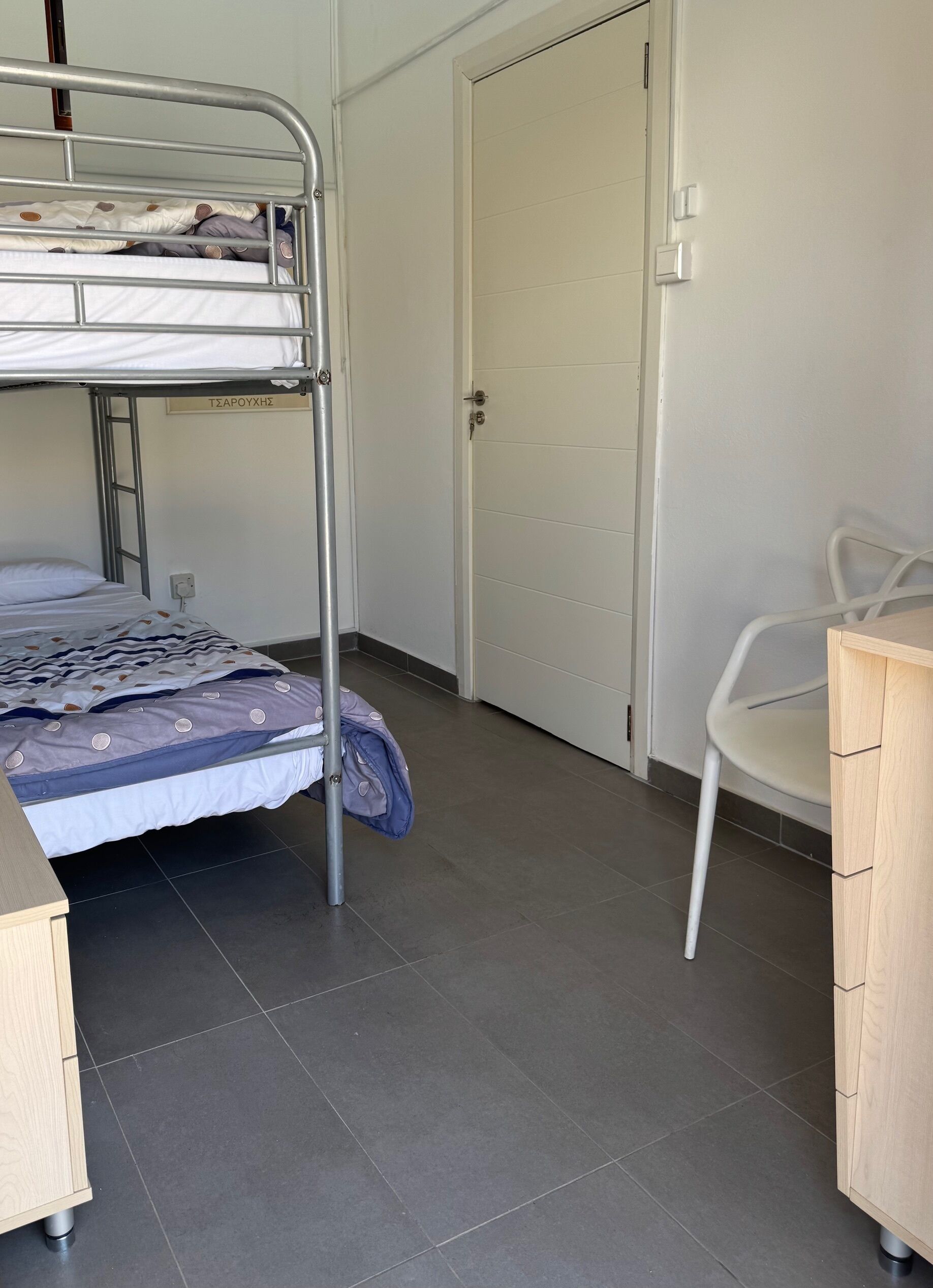 A dormitory room with a bunk bed, a desk, a chair, and a wardrobe.